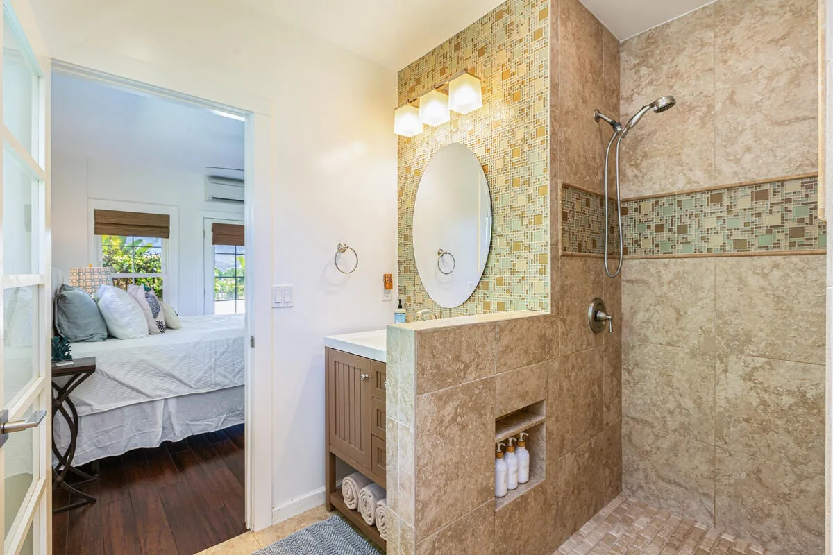 Un baño con ducha y tocador junto a una puerta abierta al dormitorio.
