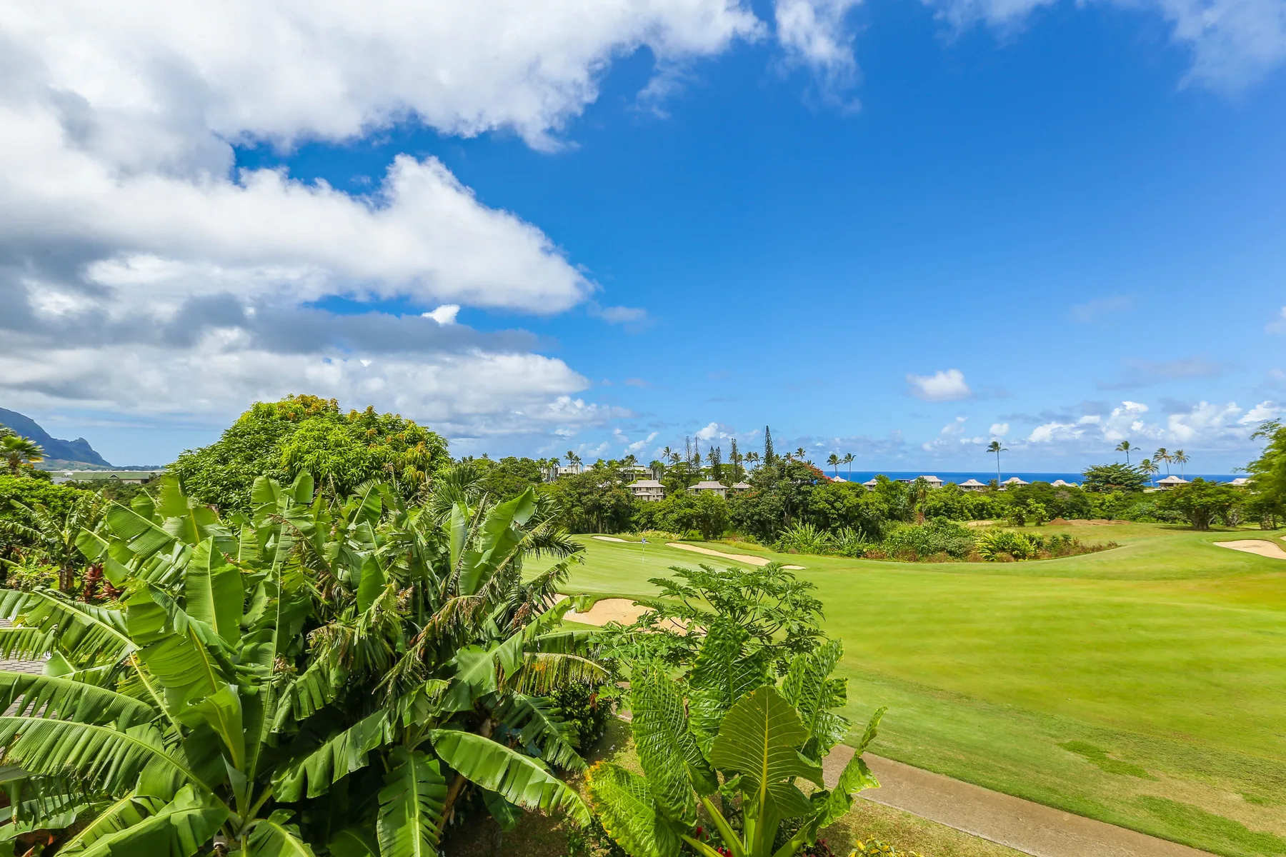 Un campo de golf tropical con zonas verdes, vegetación frondosa y vistas al océano.