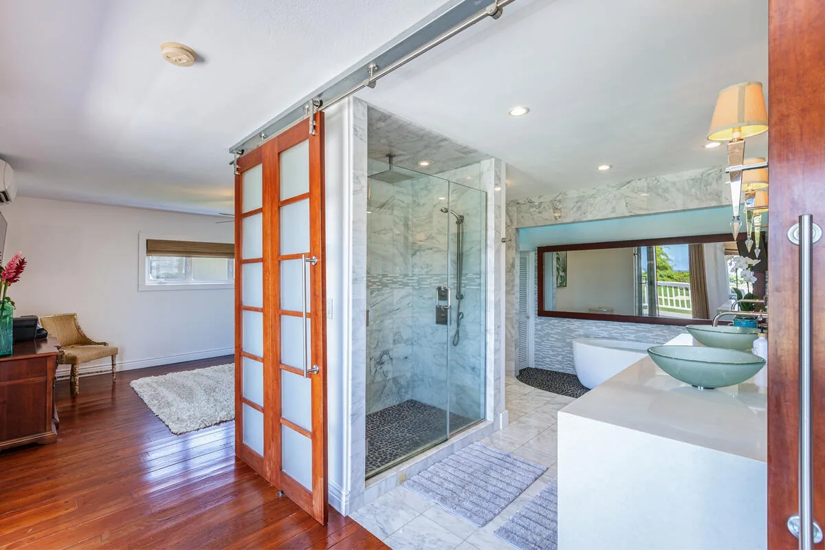 Un baño luminoso con ducha de vidrio, lavabo sobre encimera y puertas corredizas de madera abiertas.