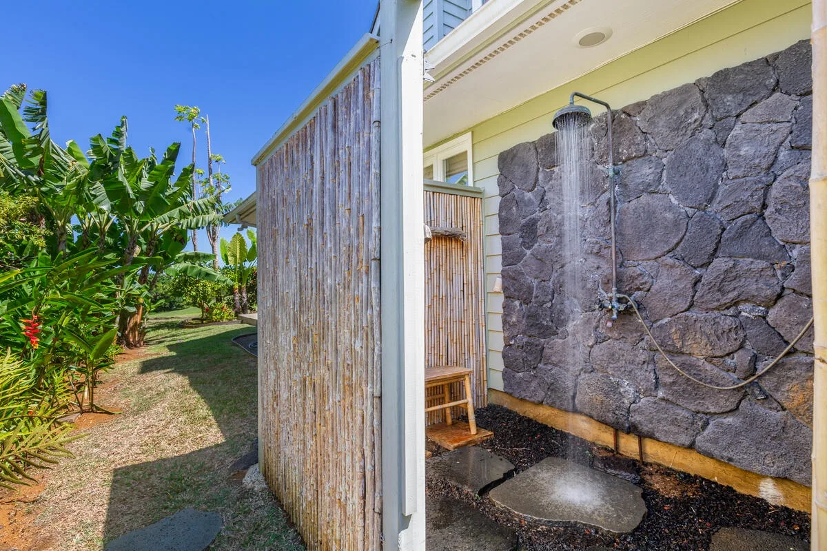 Una ducha exterior está junto a un muro de piedra y un jardín tropical.