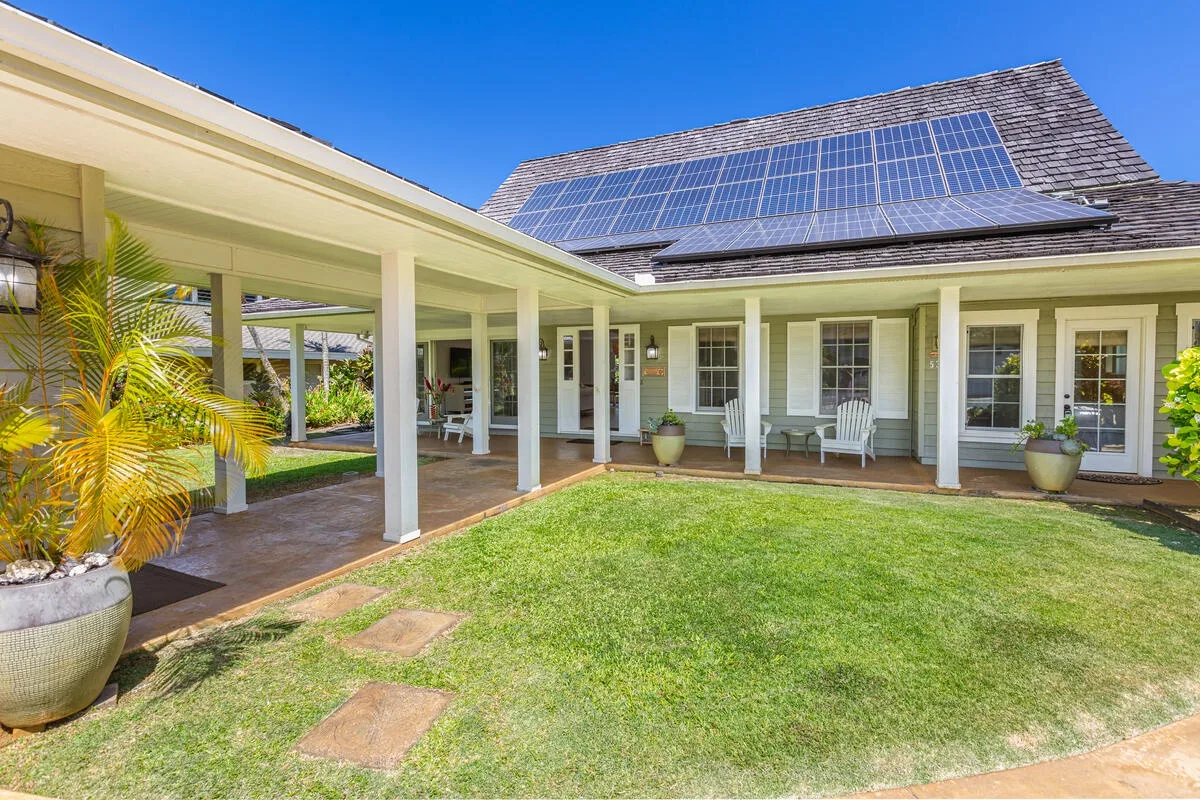 Un patio cubierto da a un jardín con césped junto a una casa con paneles solares.