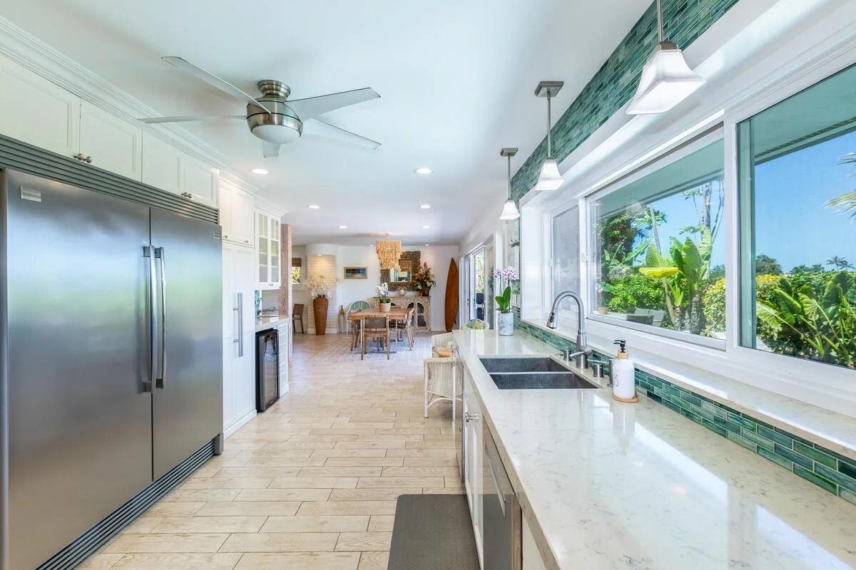Una cocina luminosa con una encimera larga y grandes ventanas con vistas a la vegetación.