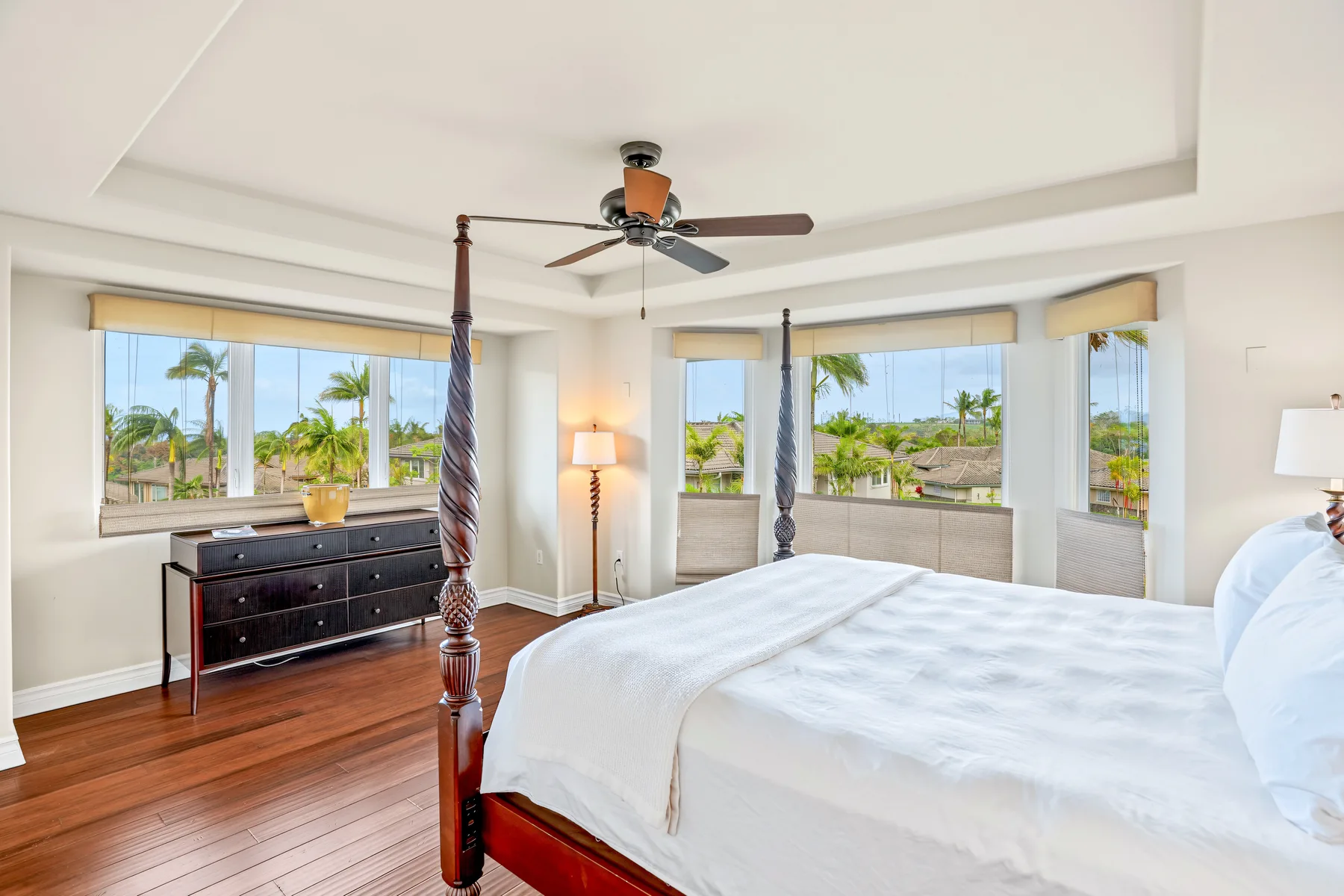A bright bedroom with a large bed and windows overlooking palm trees.