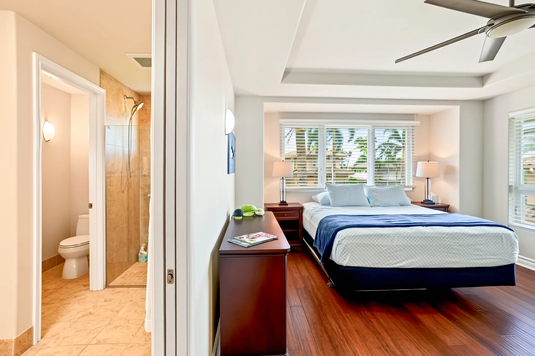 A bedroom with a bed, bedside tables, and a ceiling fan beside an adjoining bathroom.