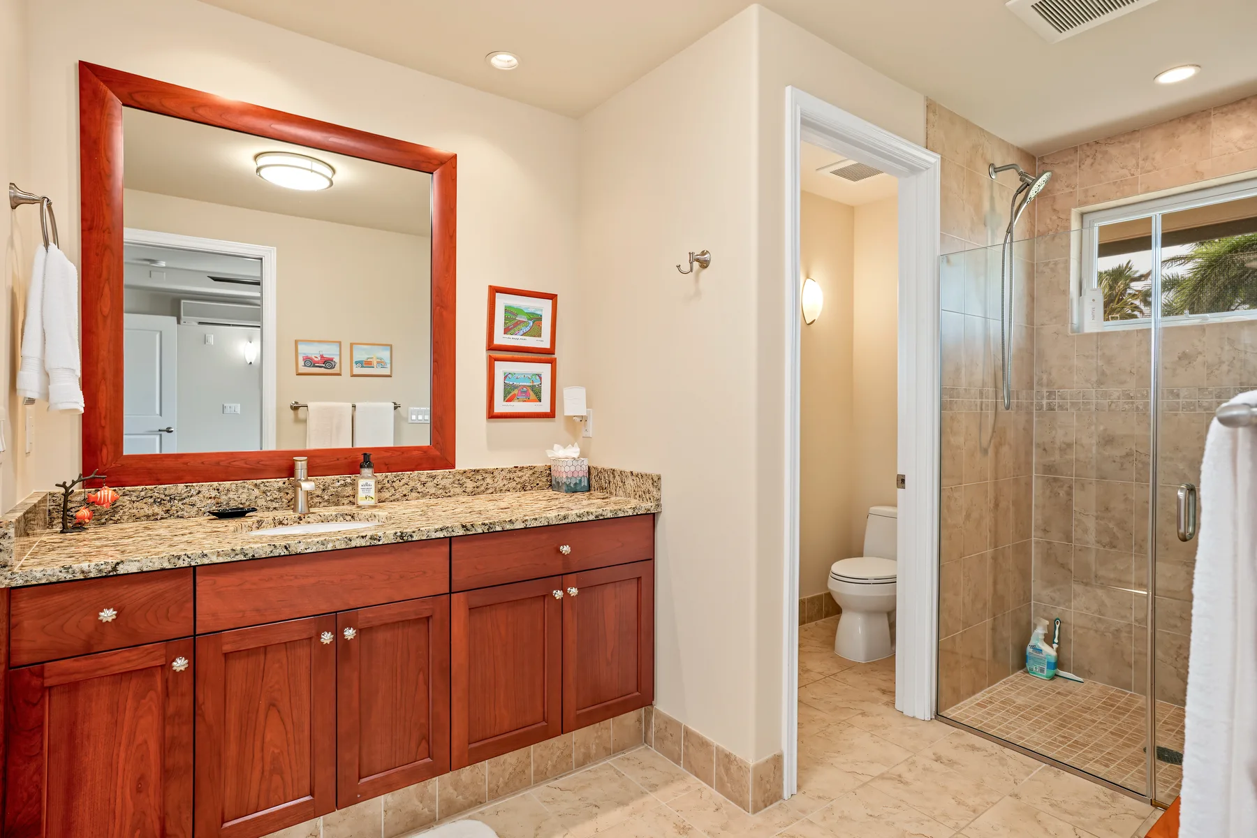 A bathroom with a long vanity, mirror, toilet, and glass shower.