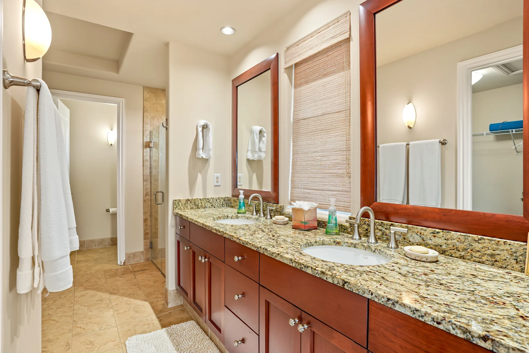 A bright bathroom with a long vanity, mirrors, and a walk-in shower.