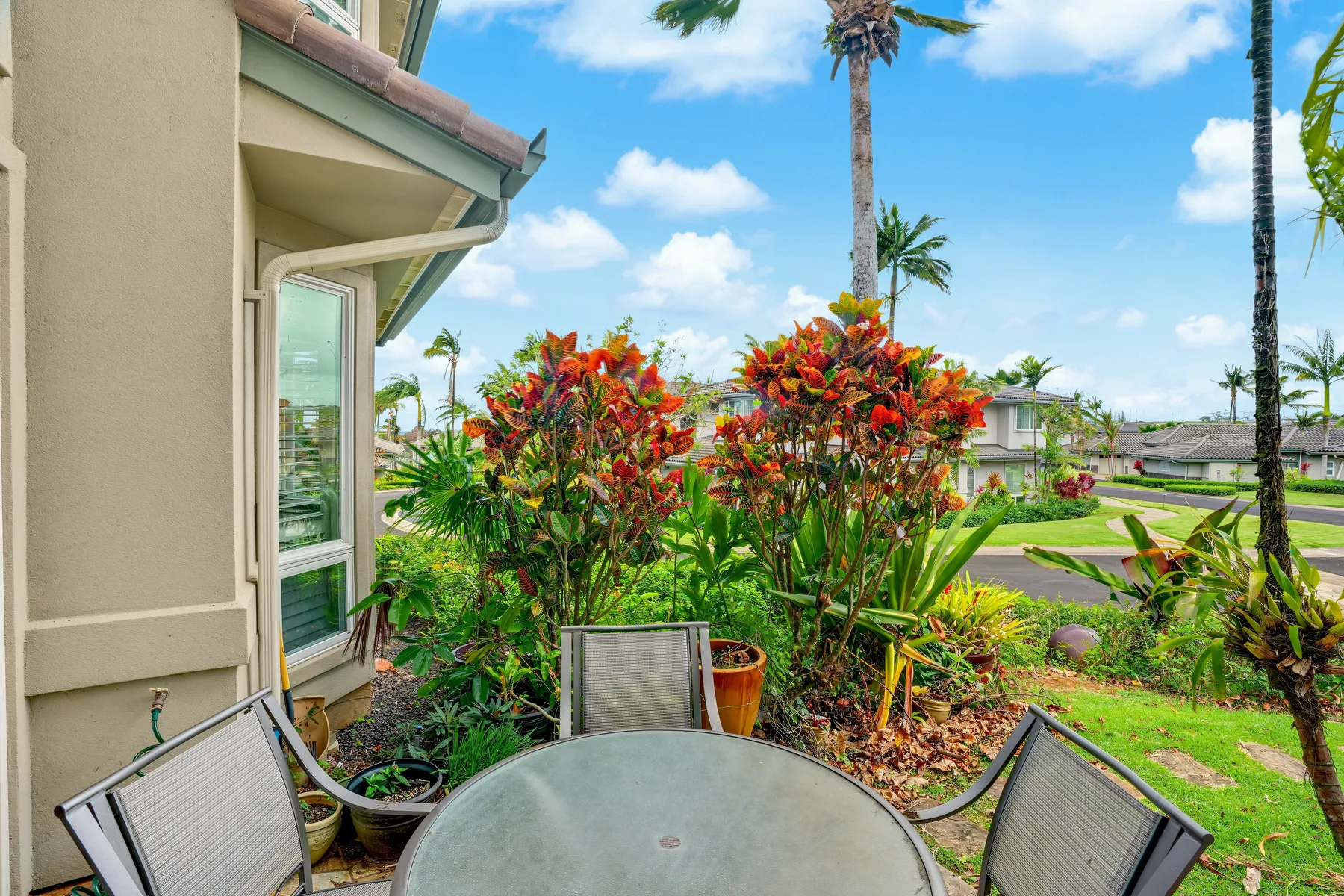 A patio seating area sits beside colorful shrubs and a grassy yard.