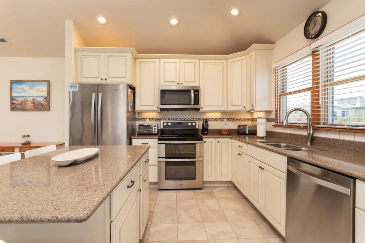 A bright kitchen with light cabinets, stainless steel appliances, and a broad countertop.