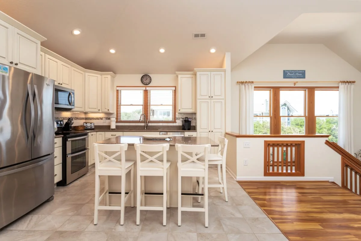 A bright kitchen with white cabinets, stainless steel appliances, and a dining island.