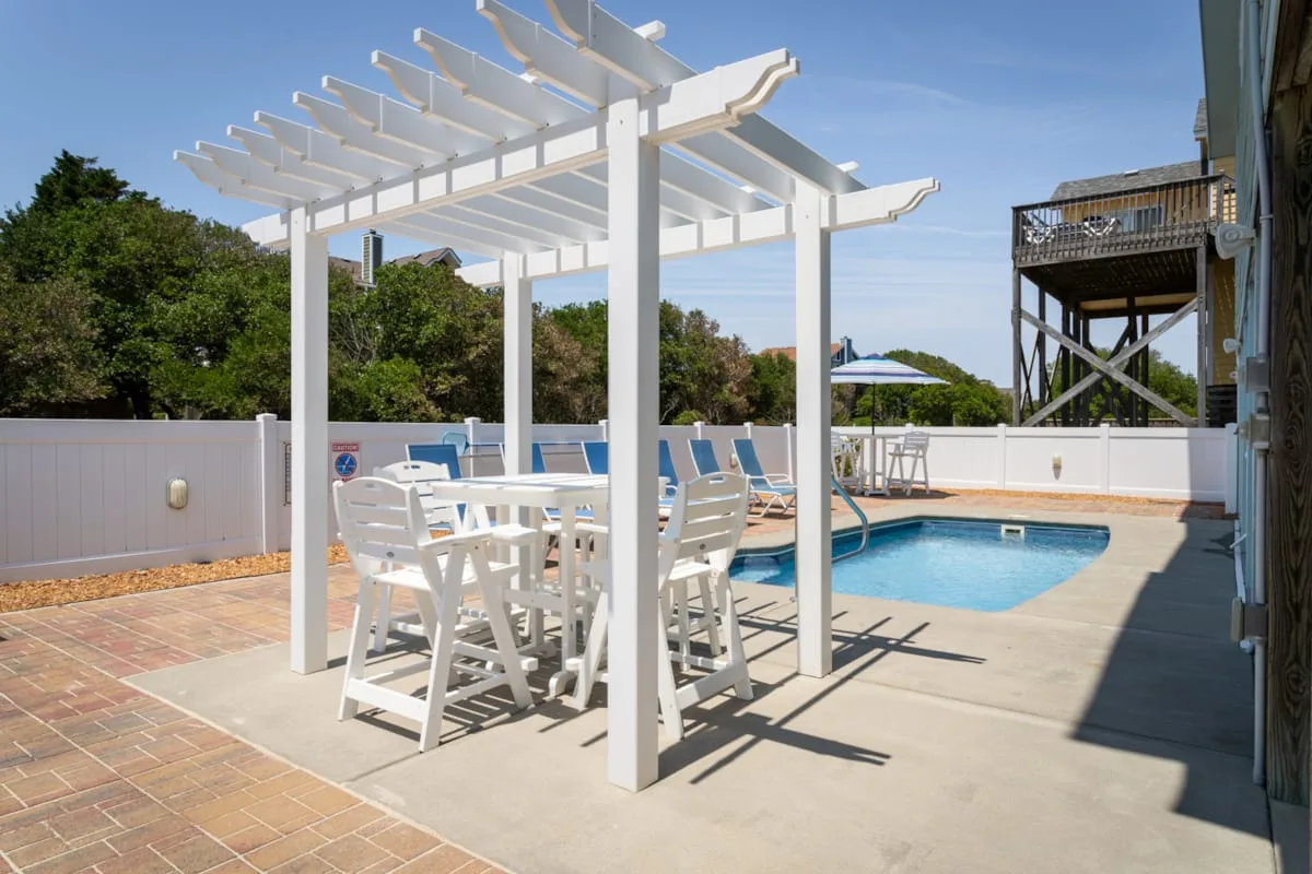 A poolside patio features white pergola seating beside a swimming pool.