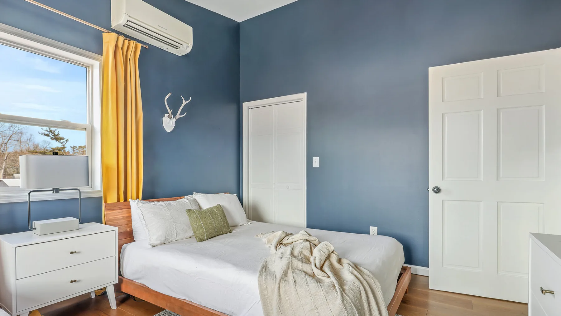 Un dormitorio con una cama, paredes azules y una ventana con cortinas amarillas.