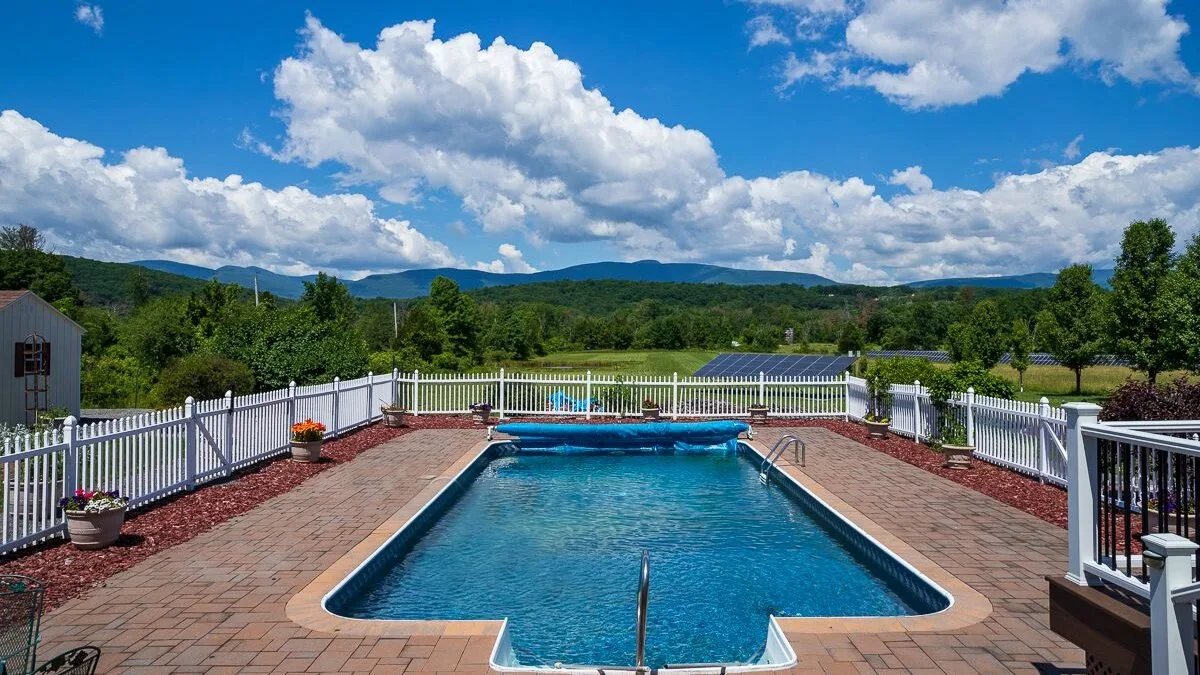 An outdoor swimming pool is surrounded by a paved deck and white railing.