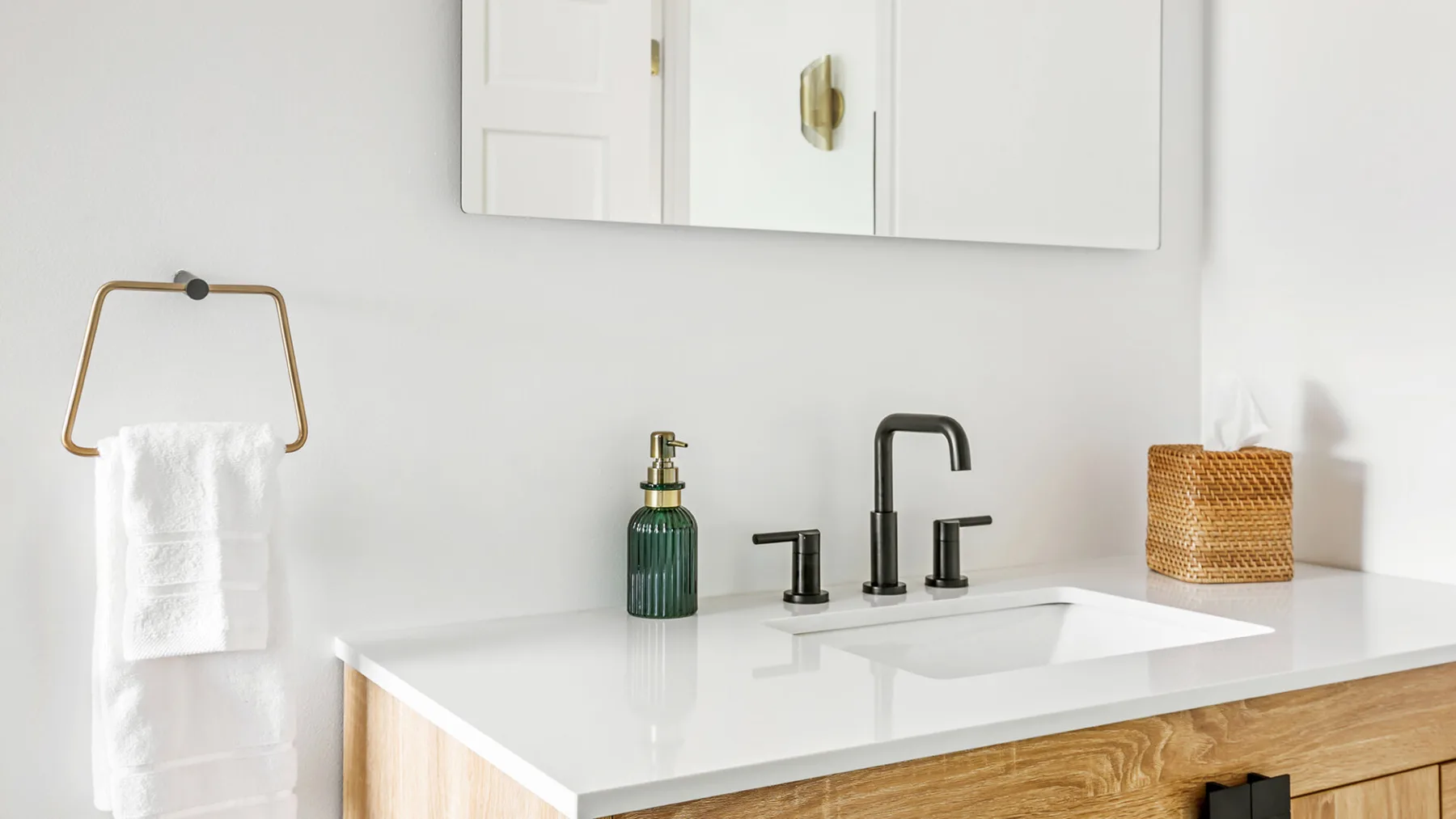 Un tocador de baño luminoso con encimera blanca, lavabo y grifo oscuro.