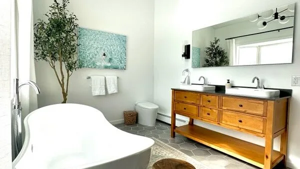 Un baño luminoso cuenta con una bañera independiente y un mueble de madera.