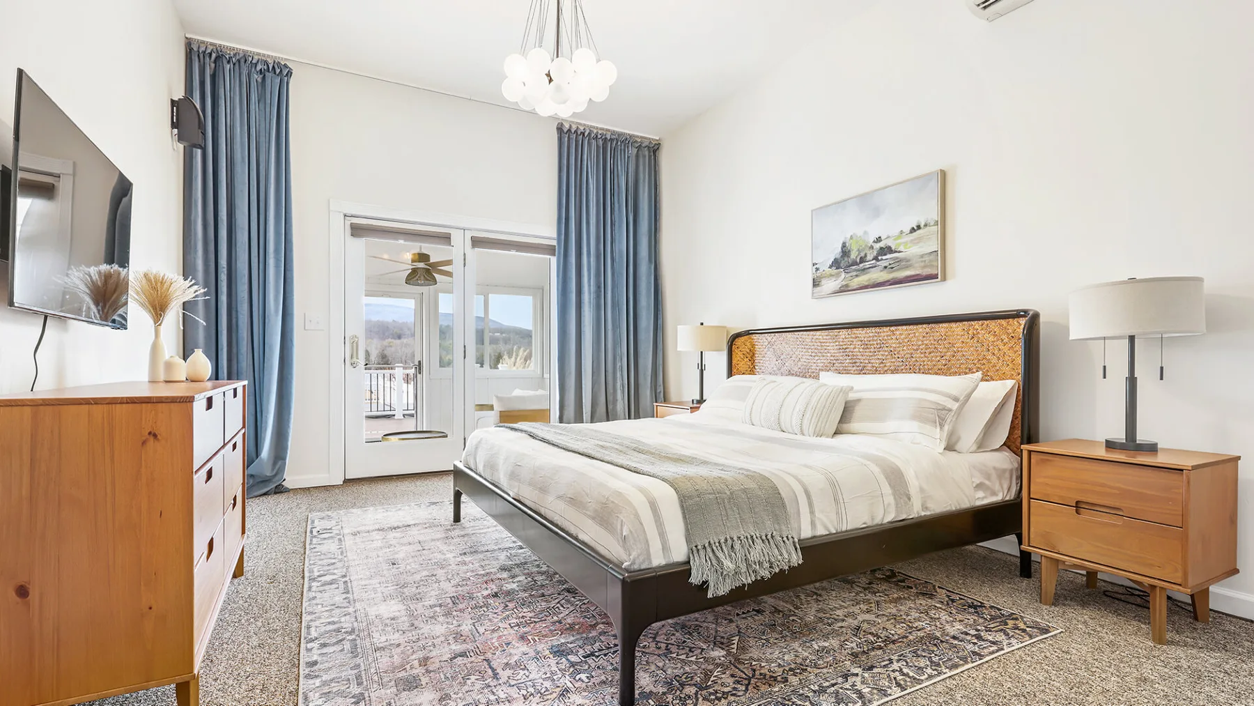 Un dormitorio con una cama grande, mesillas y cortinas azules junto a las puertas acristaladas.
