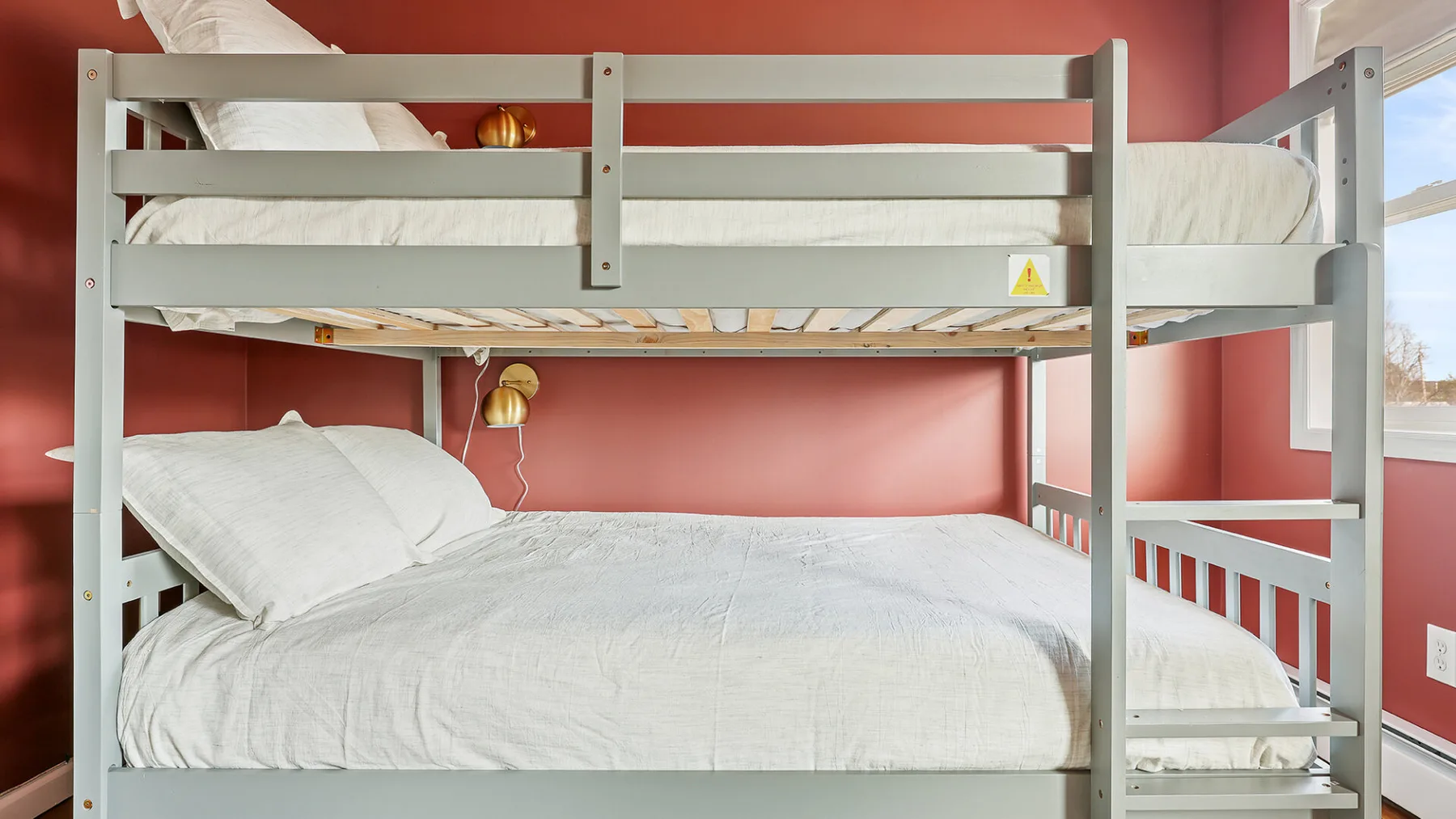 Un dormitorio con ropa de cama blanca en una litera junto a una pared rosa.