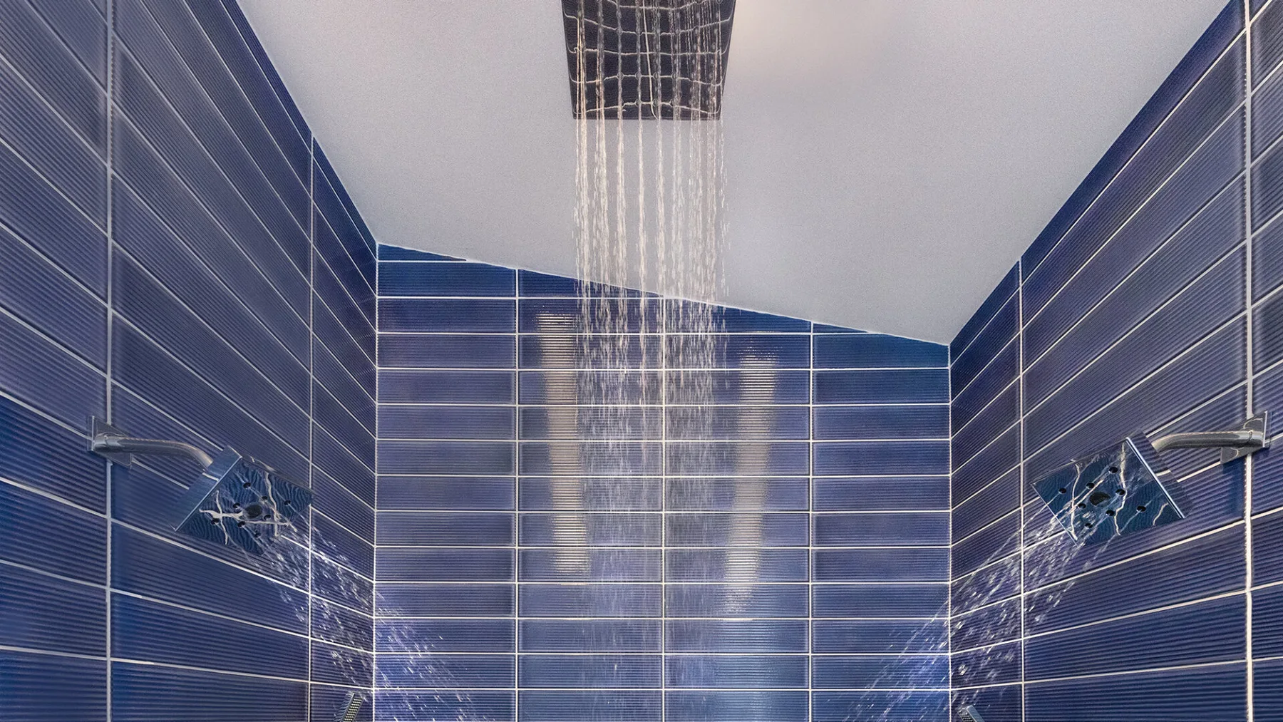 Una ducha con azulejos y agua cayendo desde una alcachofa superior.