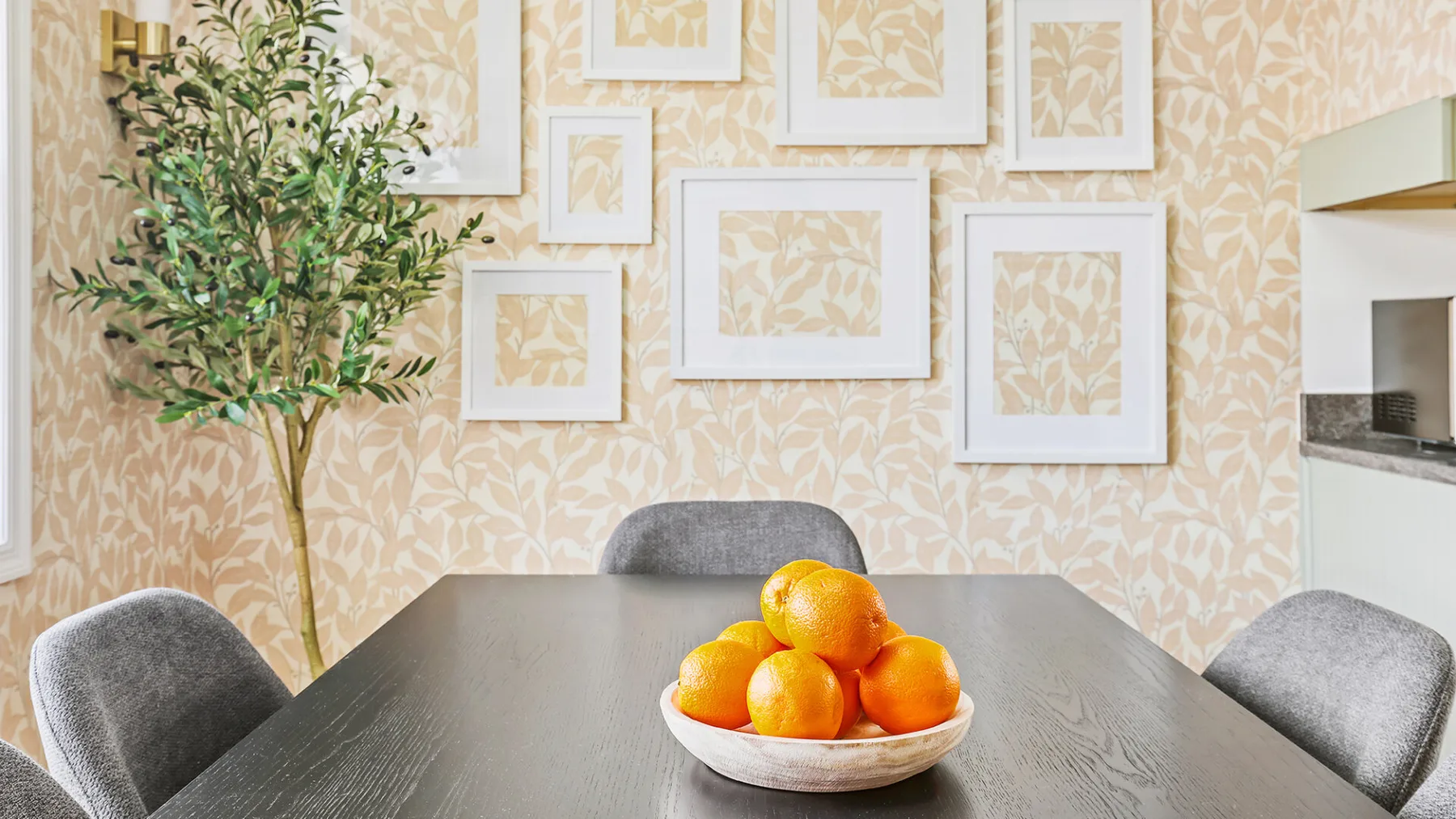 Una mesa de comedor con un cuenco de naranjas está frente a cuadros en la pared.