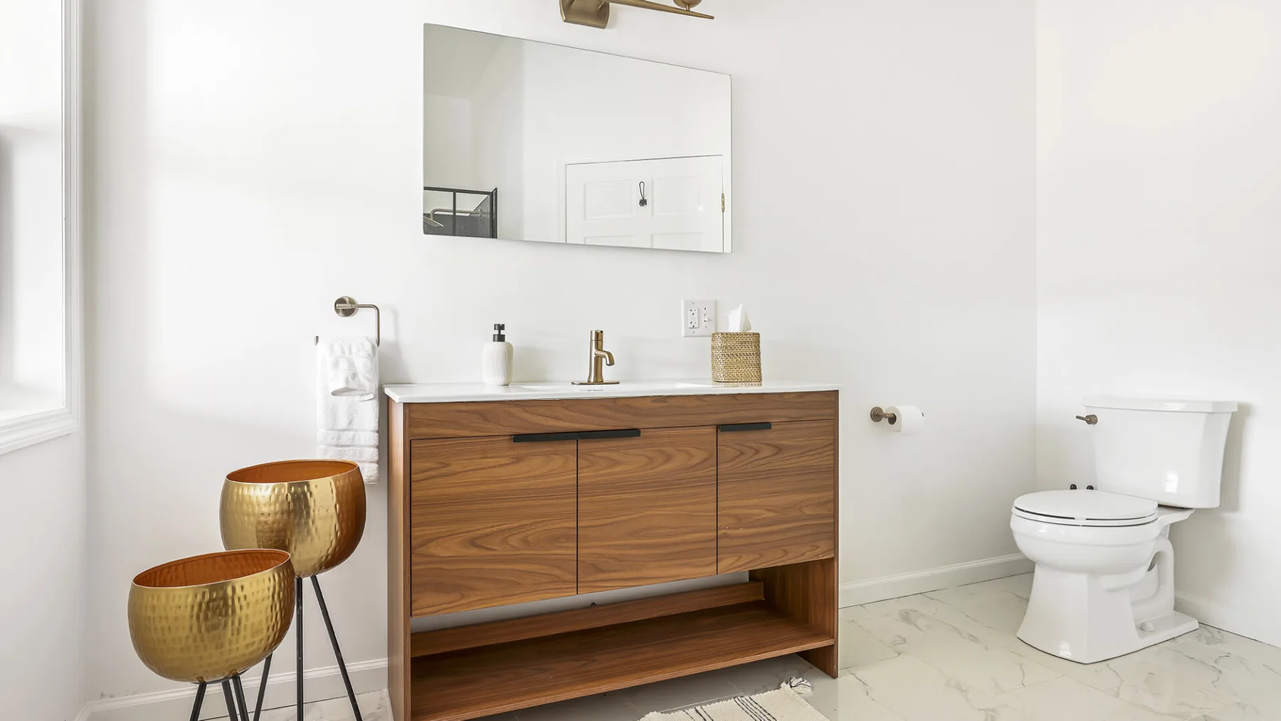 Un baño luminoso tiene un tocador de madera, un espejo de pared y un inodoro.