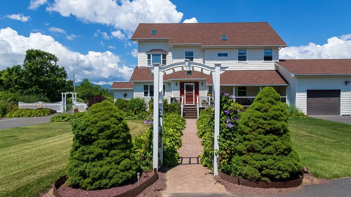 Una casa grande se encuentra detrás de un jardín paisajístico y un sendero central.