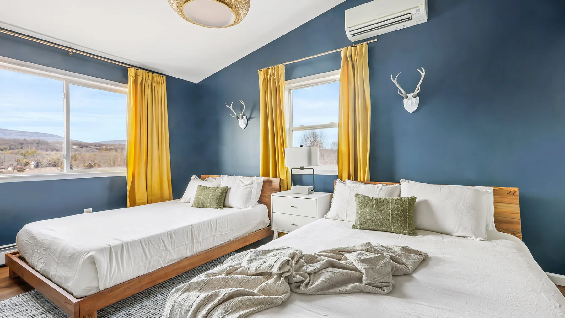 Un dormitorio con dos camas, ropa de cama blanca y cortinas amarillas sobre paredes azules.