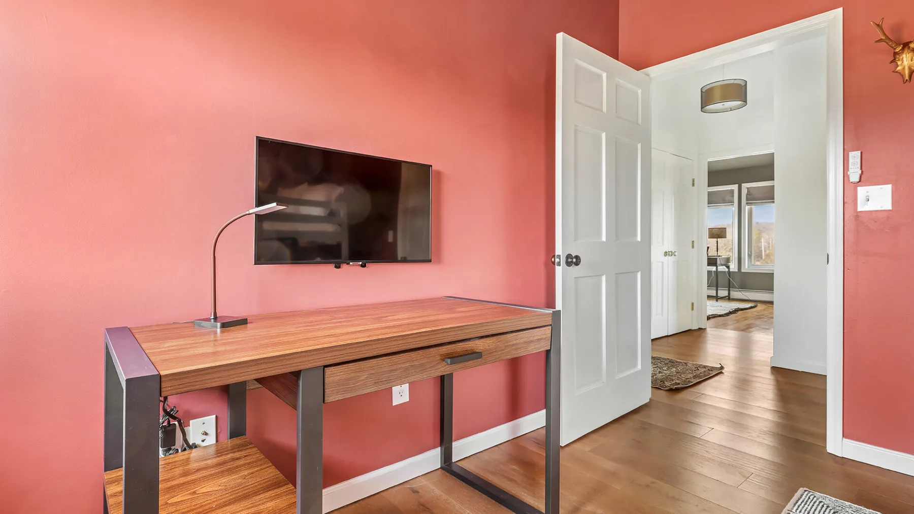 Una habitación color coral con un escritorio de madera y un televisor en la pared.