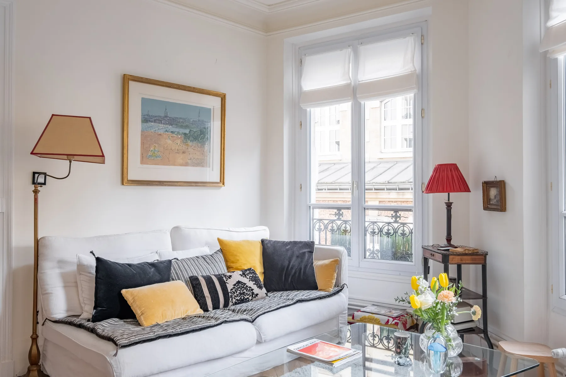 Una sala luminosa con un sofá blanco y ventanas altas.