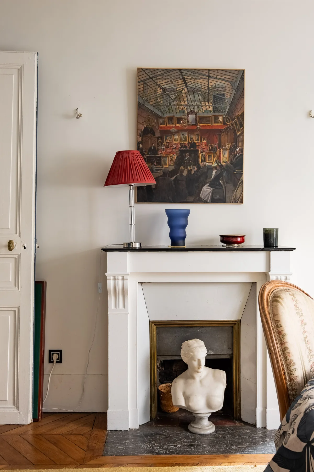 Una sala de estar tiene una chimenea blanca con un busto y un cuadro enmarcado encima.