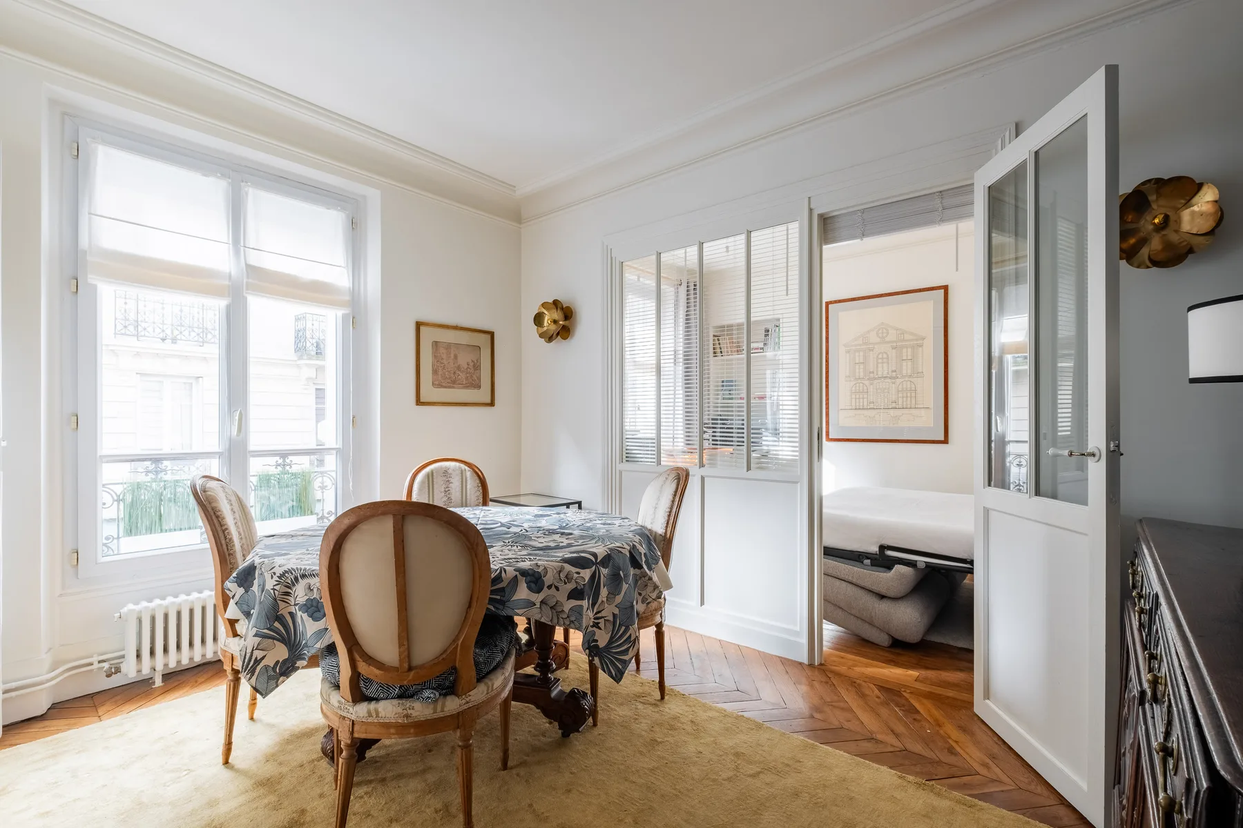 Un comedor luminoso con una mesa junto a grandes ventanas y puertas interiores abiertas.