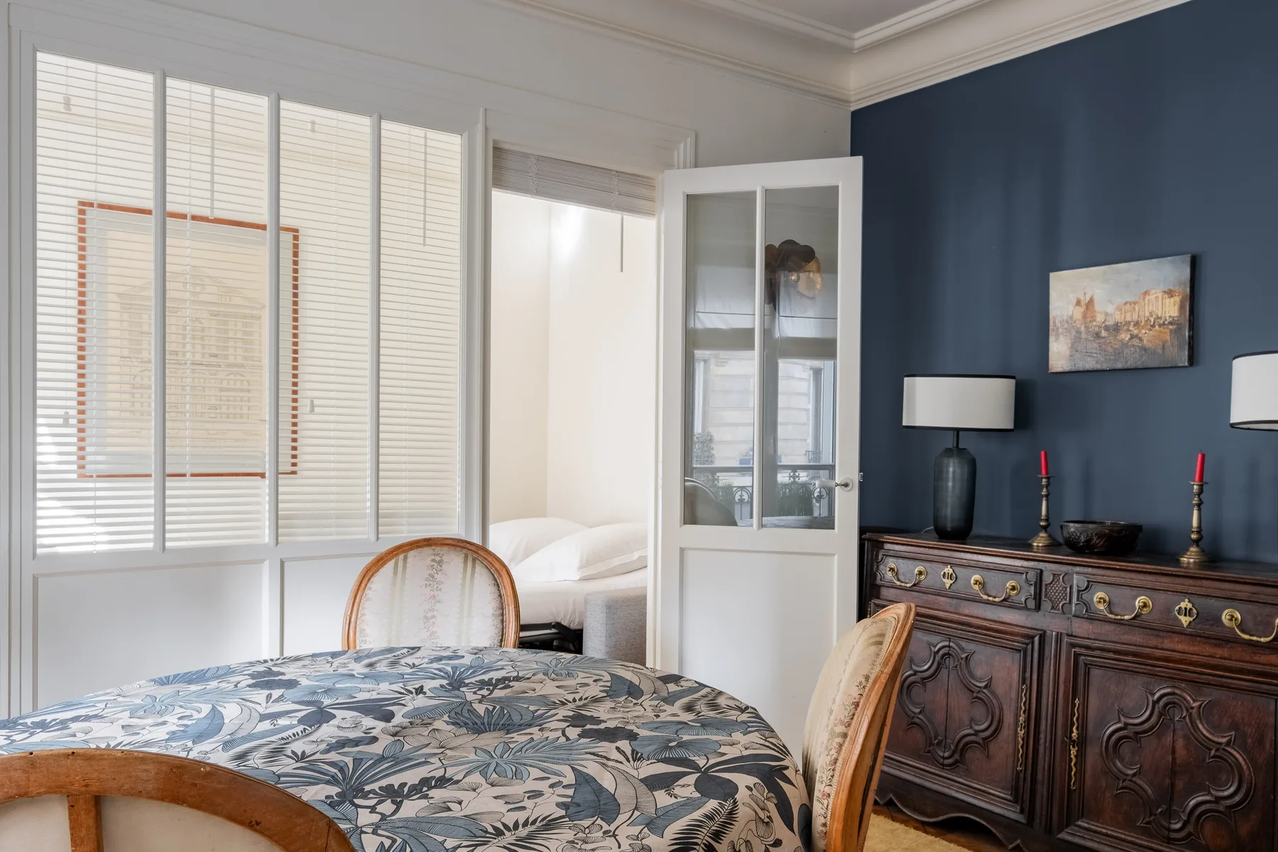 A bedroom with a patterned bedspread, bright windows, and a dark wooden dresser.