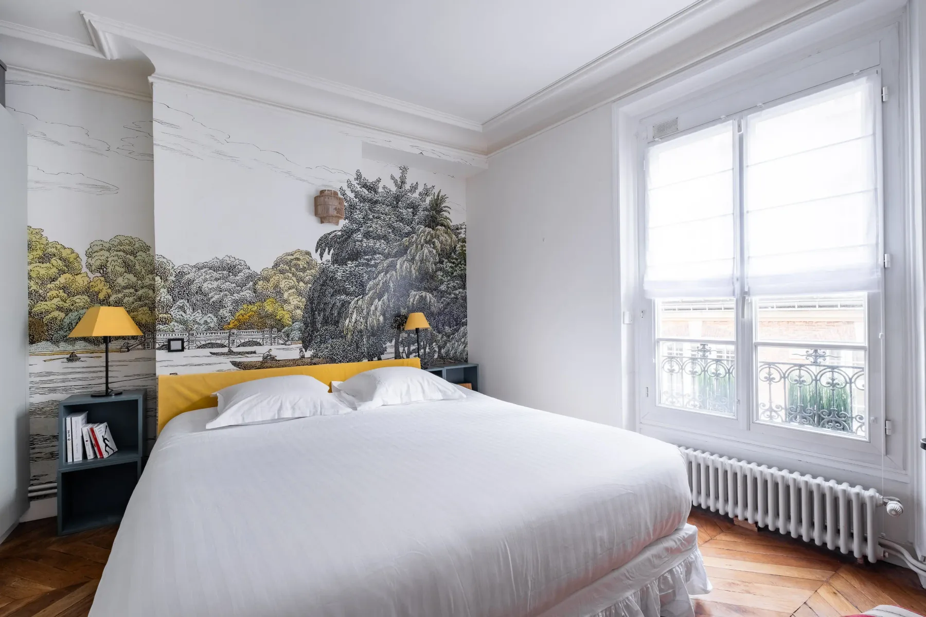 A bright bedroom with a bed, woodland mural, and large windows.