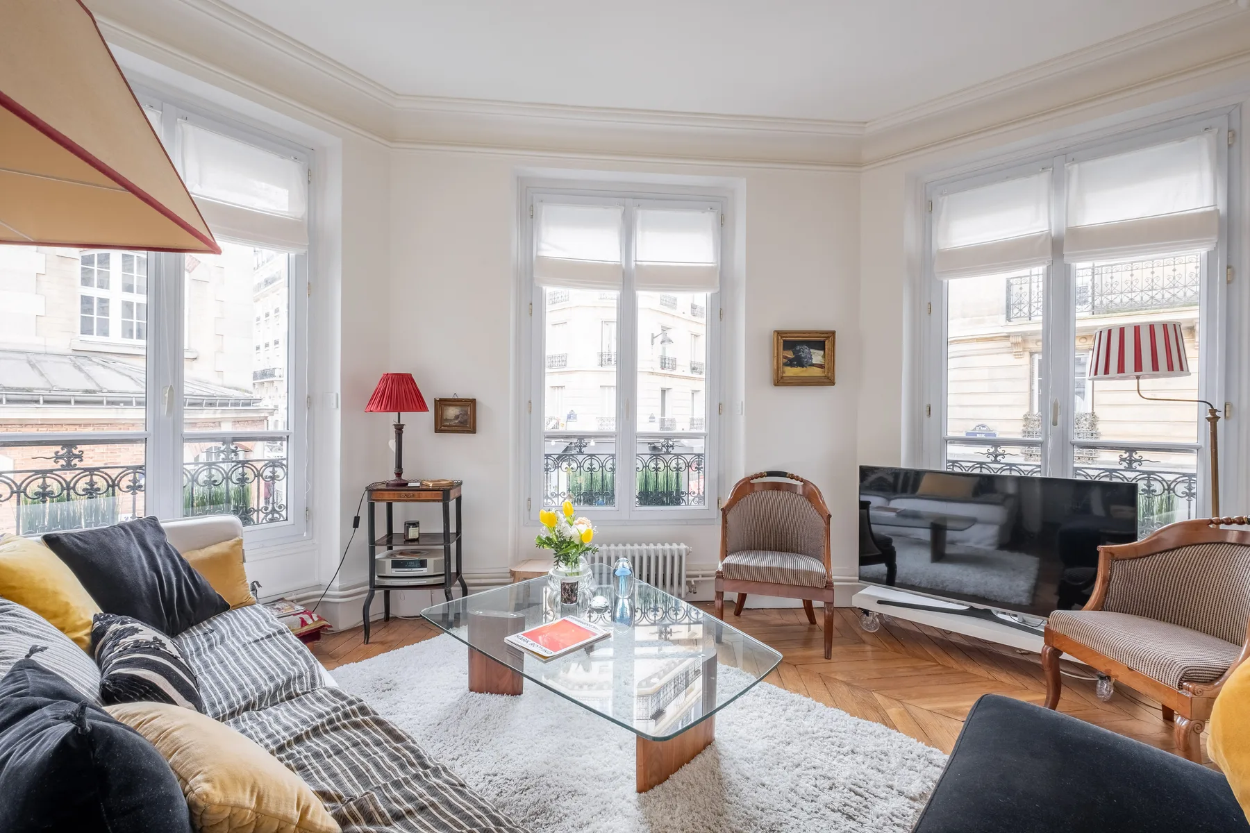 Una sala de estar luminosa con una mesa de centro de vidrio y asientos junto a grandes ventanas.