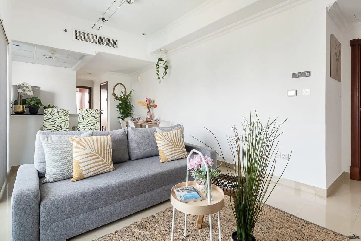 Una sala luminosa con asientos grises, cojines decorativos y plantas de interior.
