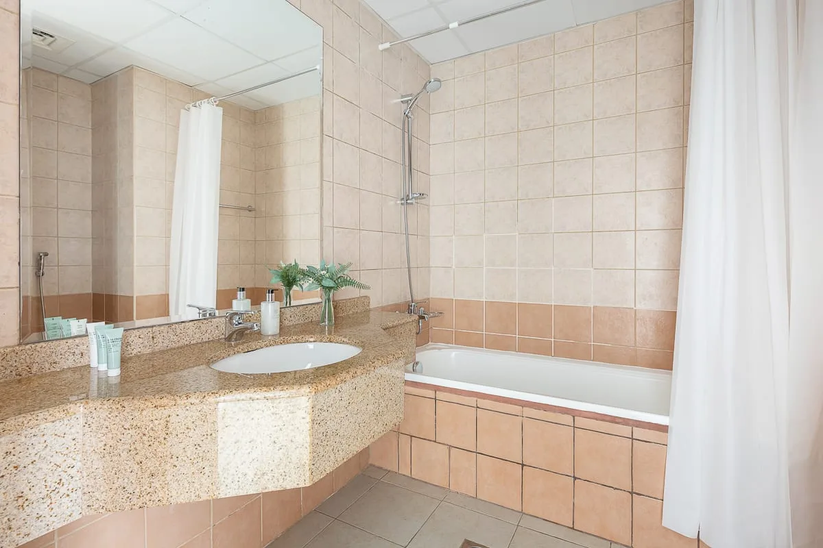 Un baño alicatado con una amplia encimera de lavabo y una bañera.