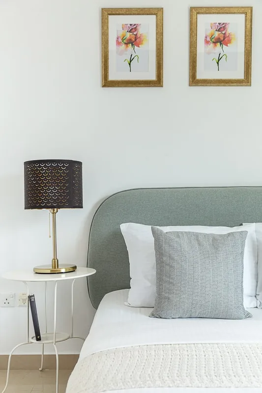 Un dormitorio con cama, mesa auxiliar, lámpara y cuadros florales.