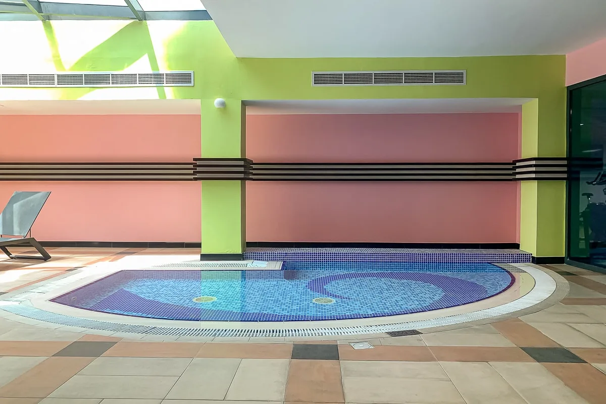 Una piscina cubierta con una sección circular de azulejos azules está junto a paredes rosas y verdes.
