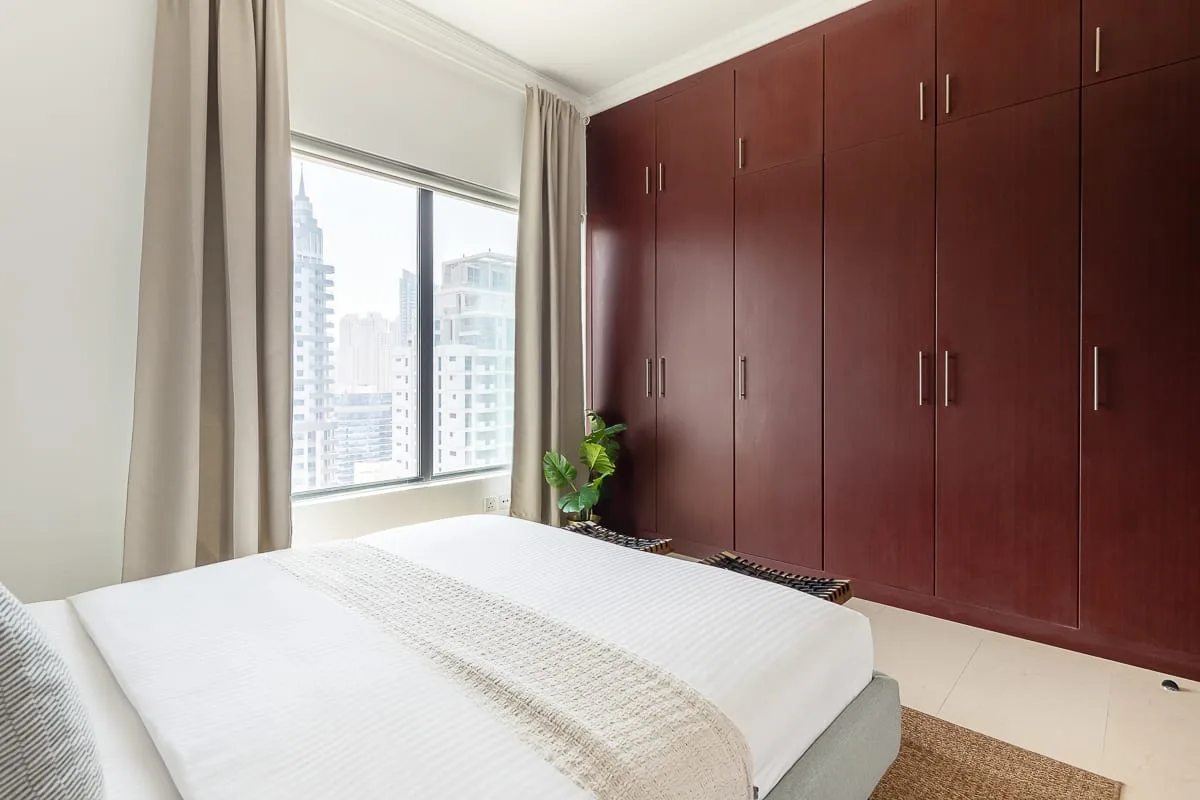 Un dormitorio con una cama bien hecha, una ventana amplia y armarios empotrados.
