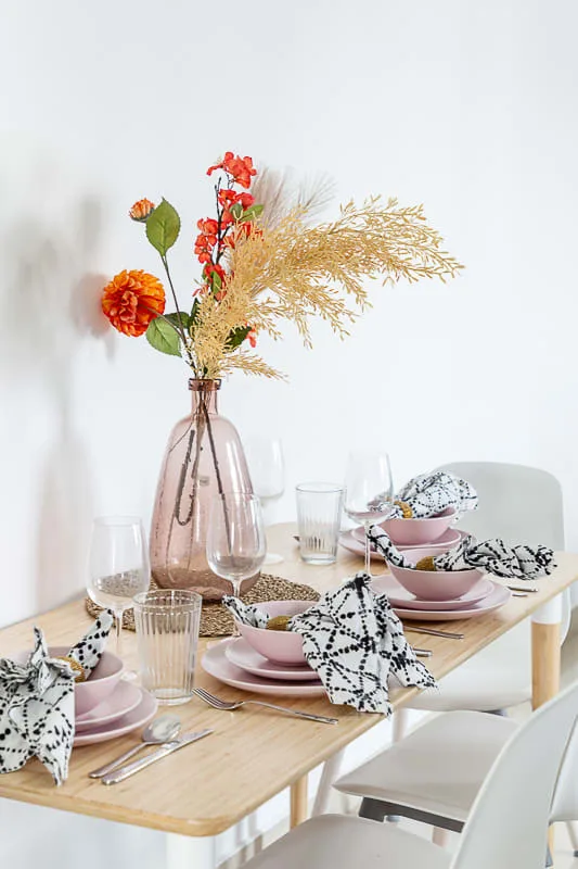 Una mesa de comedor está puesta con platos, vasos y un jarrón con flores.