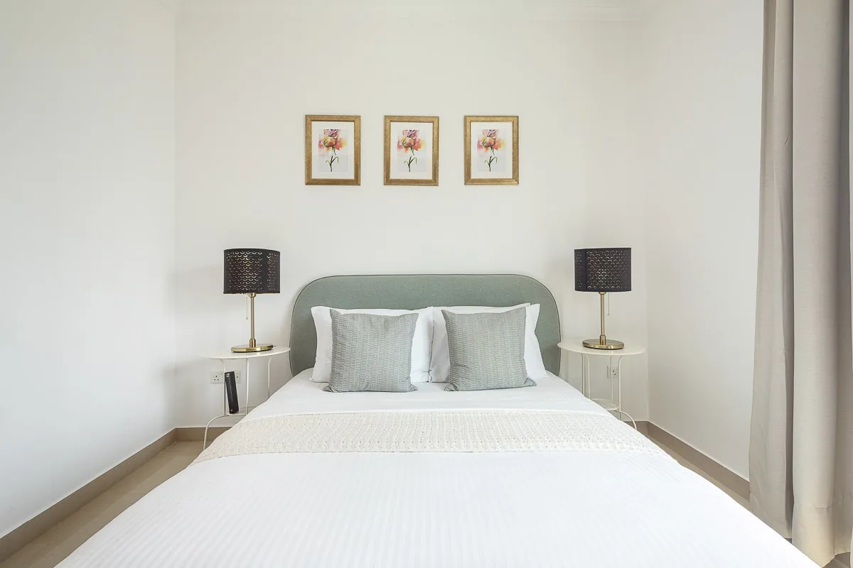 Un dormitorio luminoso con una cama bien tendida y cuadros florales sobre el cabecero.