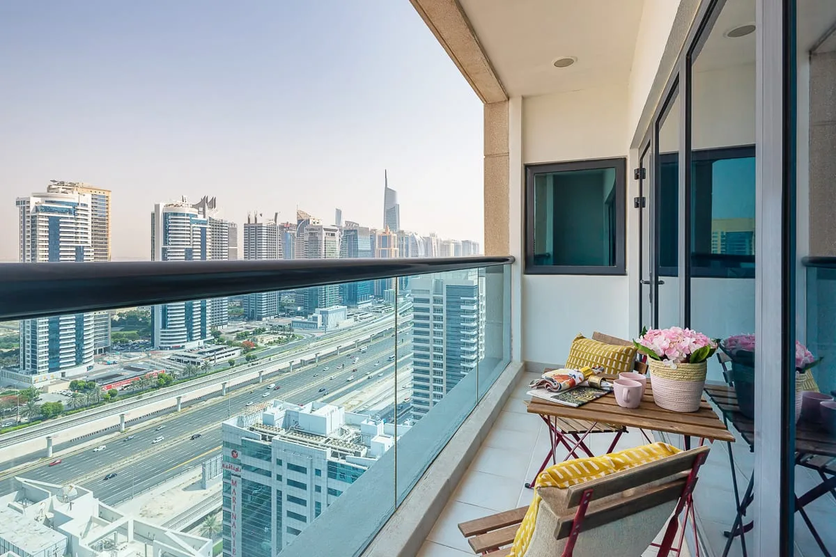 Un balcón con una mesa pequeña y asientos tiene vistas al horizonte de la ciudad.
