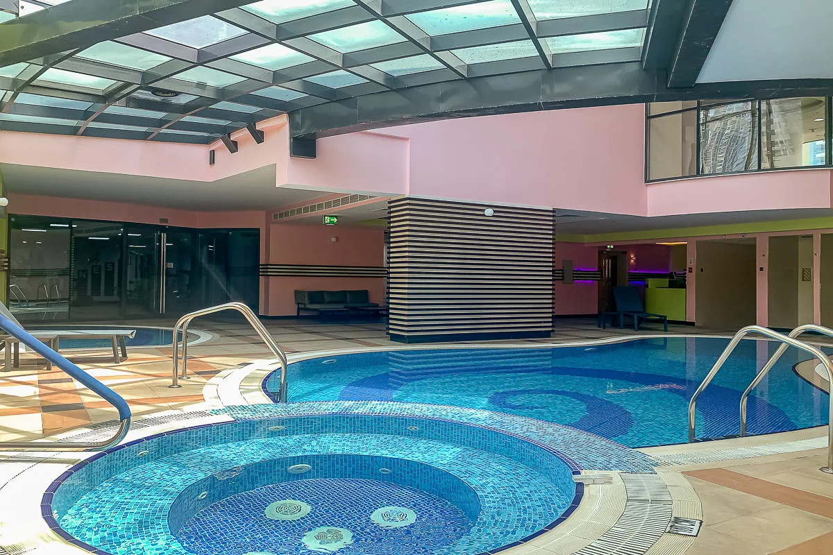 Una piscina cubierta con mosaicos azules bajo un techo de vidrio.