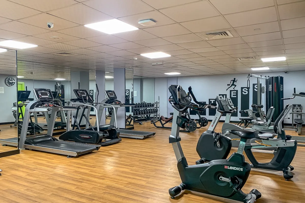 Un gimnasio con máquinas de ejercicio y pesas sobre un suelo de aspecto madera.