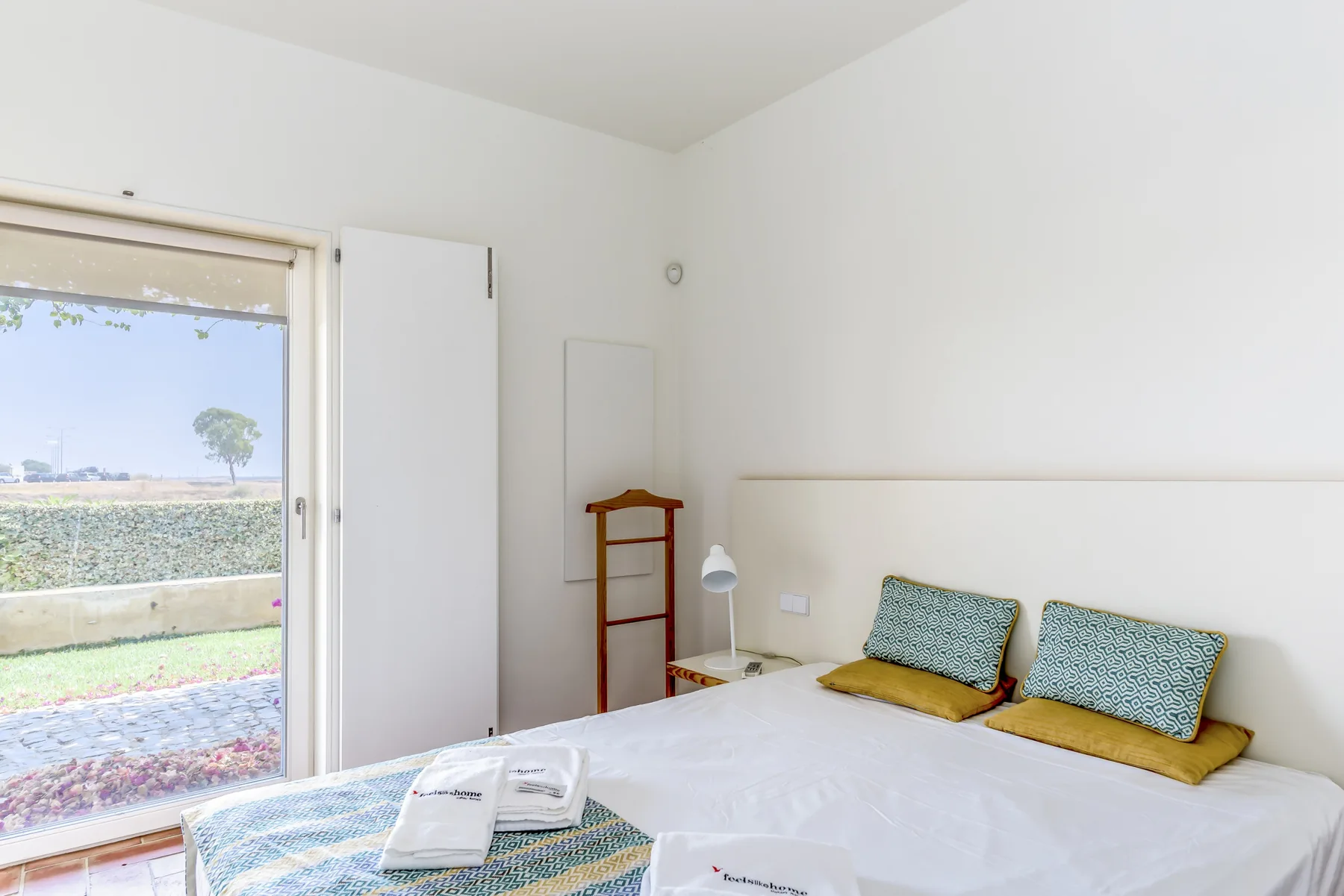A bright bedroom with a bed, bedside table, and open balcony doorway.