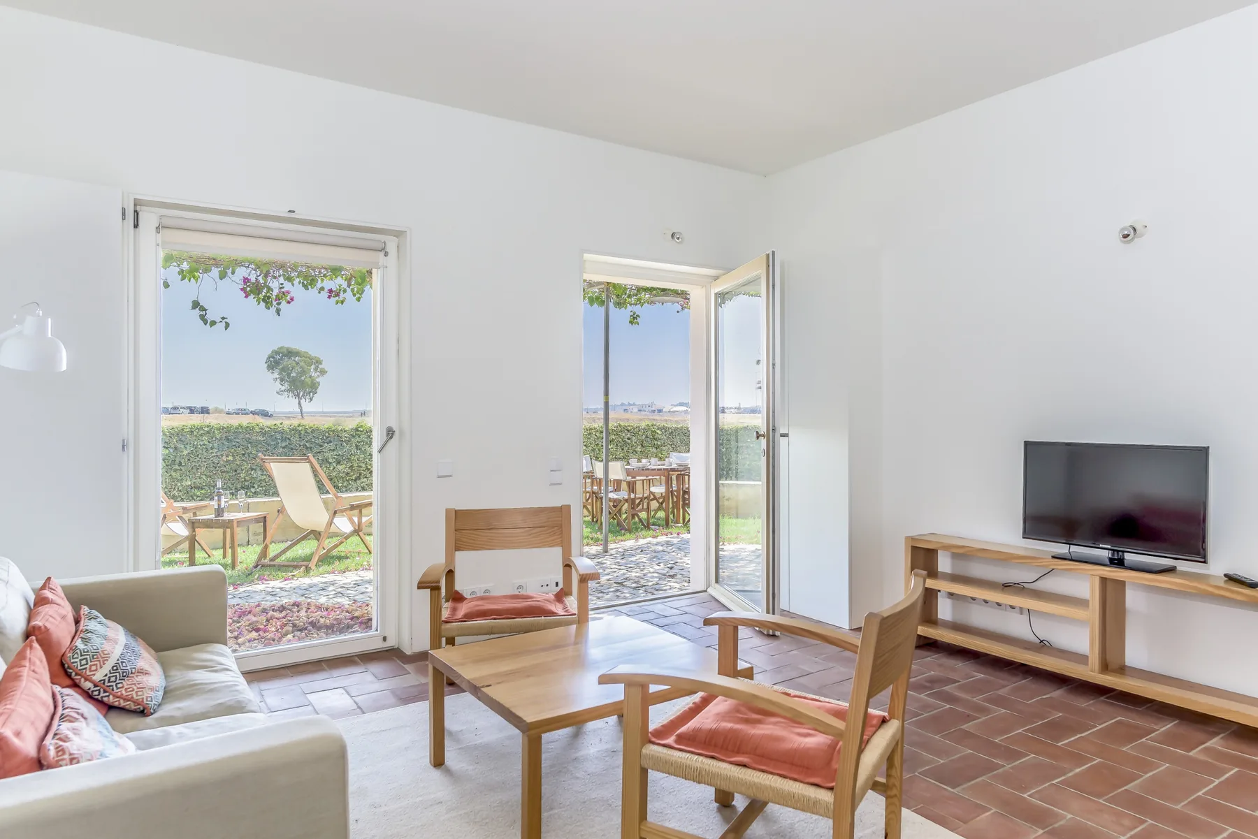 A bright living room opens onto a patio, with seating and a television.