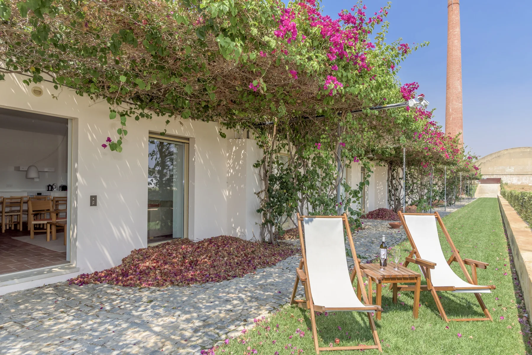 A garden patio with reclining seating beneath flowering vines.