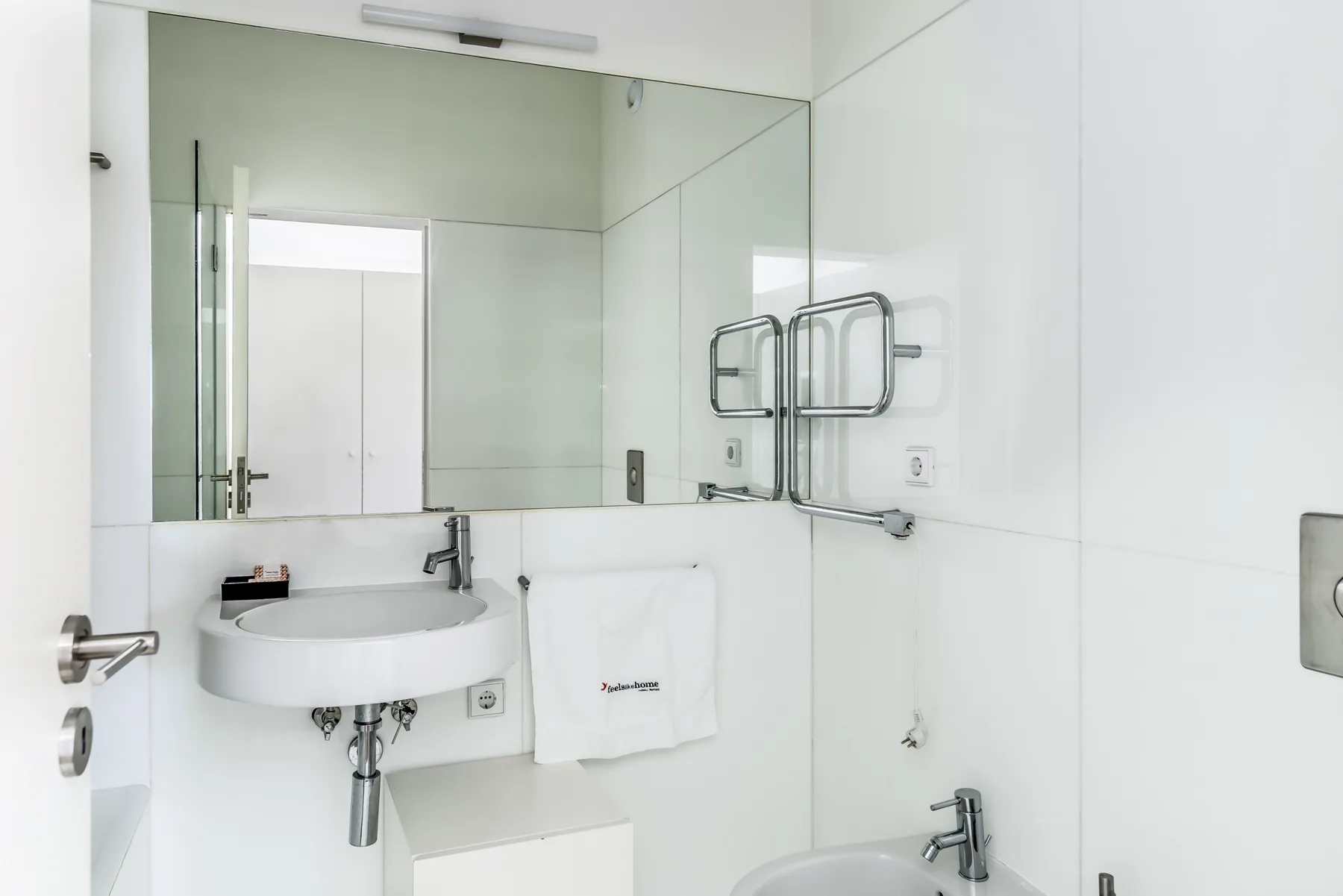 A bright white bathroom with a wall-mounted sink and large mirror.