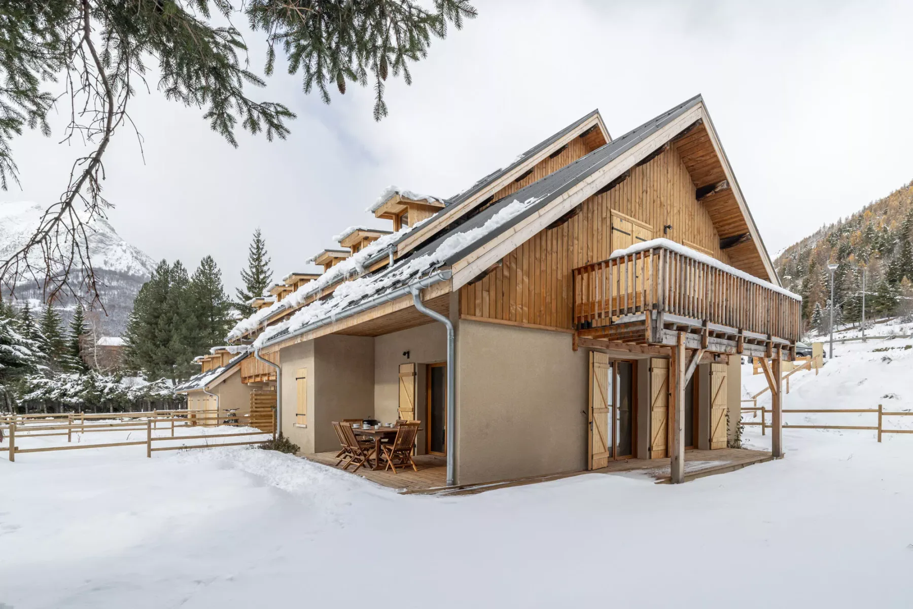 A chalet-style building stands in a snowy landscape, with a wooden balcony.