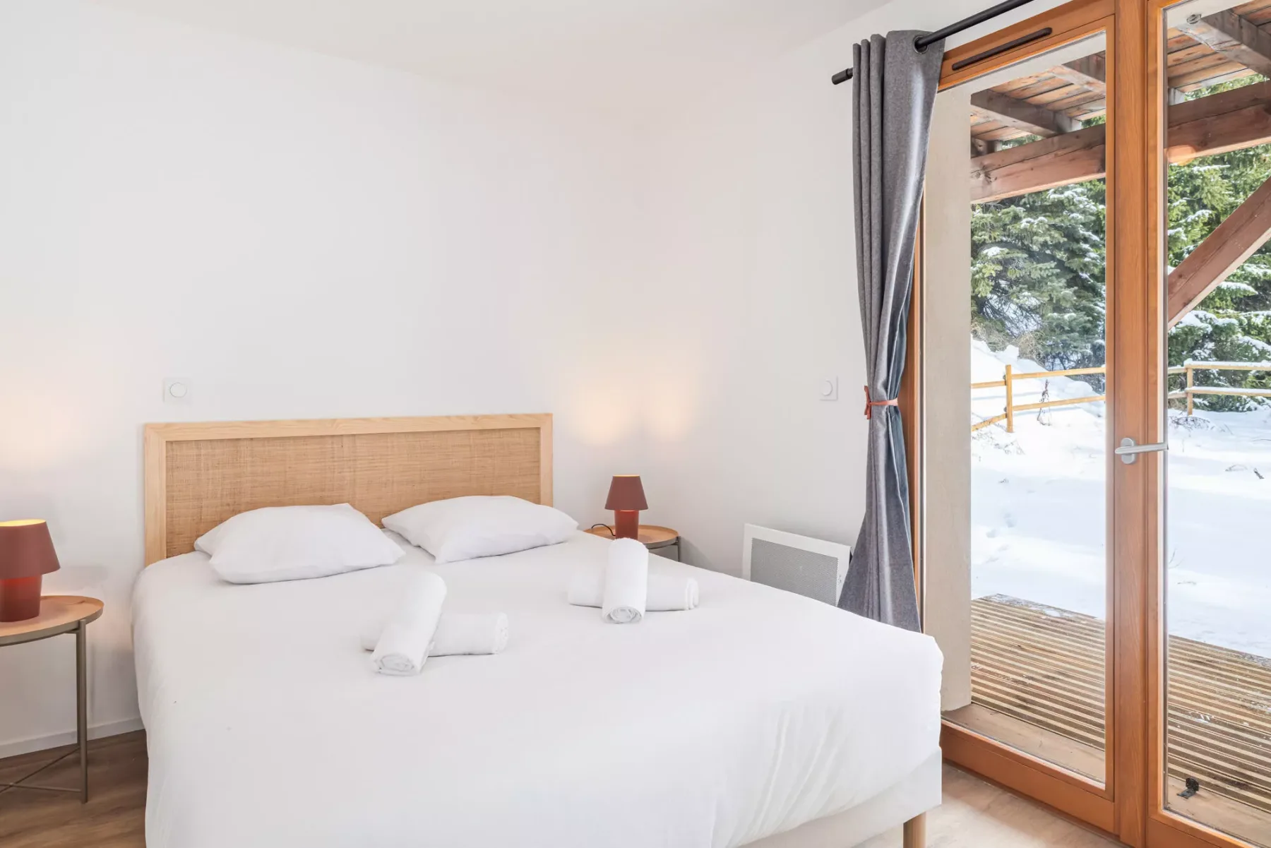 A bright bedroom with white bedding and a glass door opening onto a snowy view.