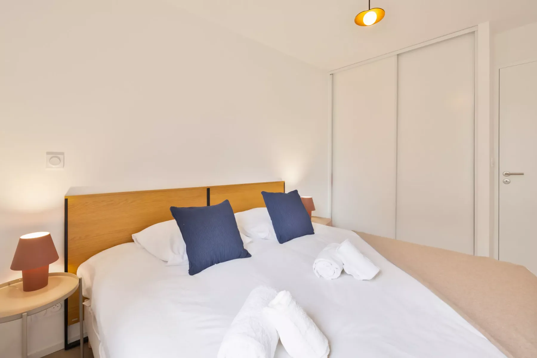 A bedroom with a double bed, white bedding, and dark accent pillows.