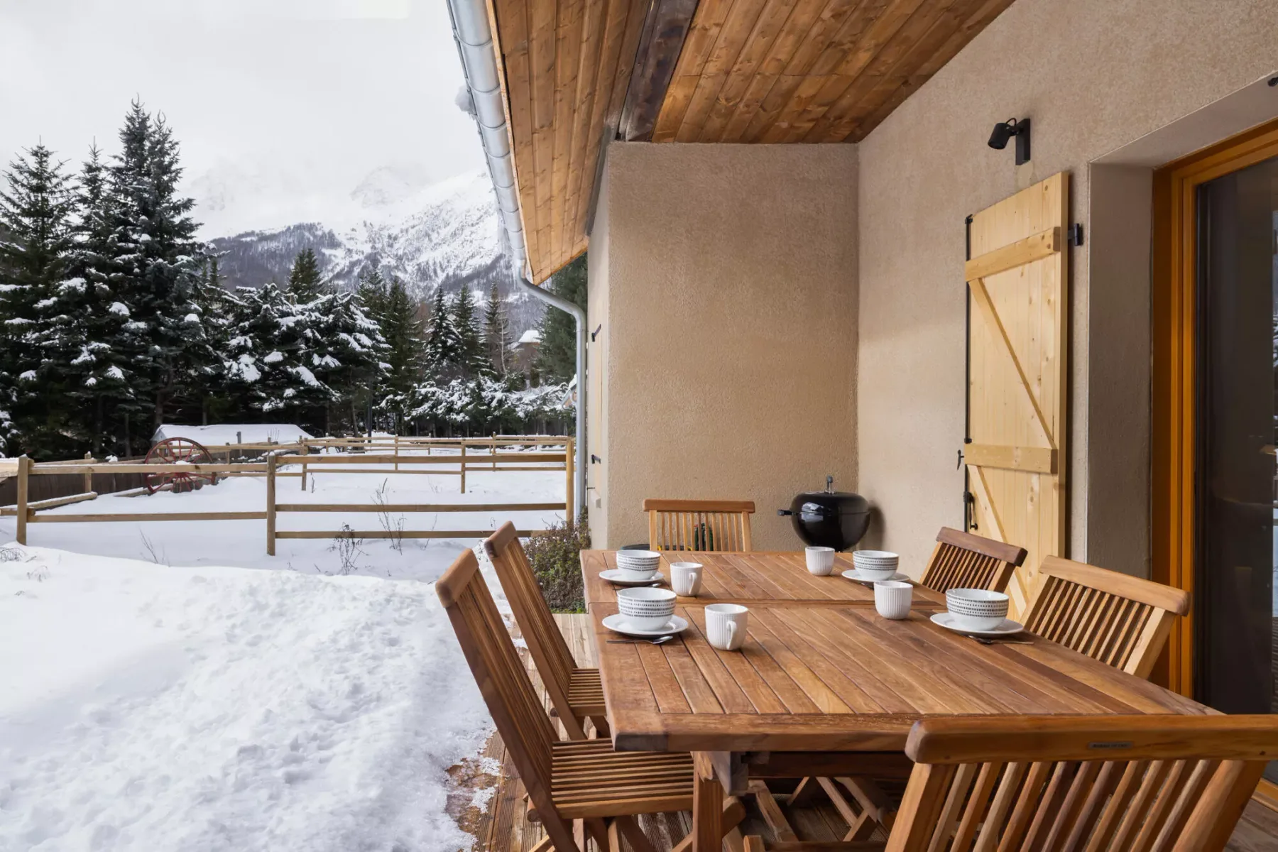 A wooden outdoor dining area opens onto a snowy mountain view.
